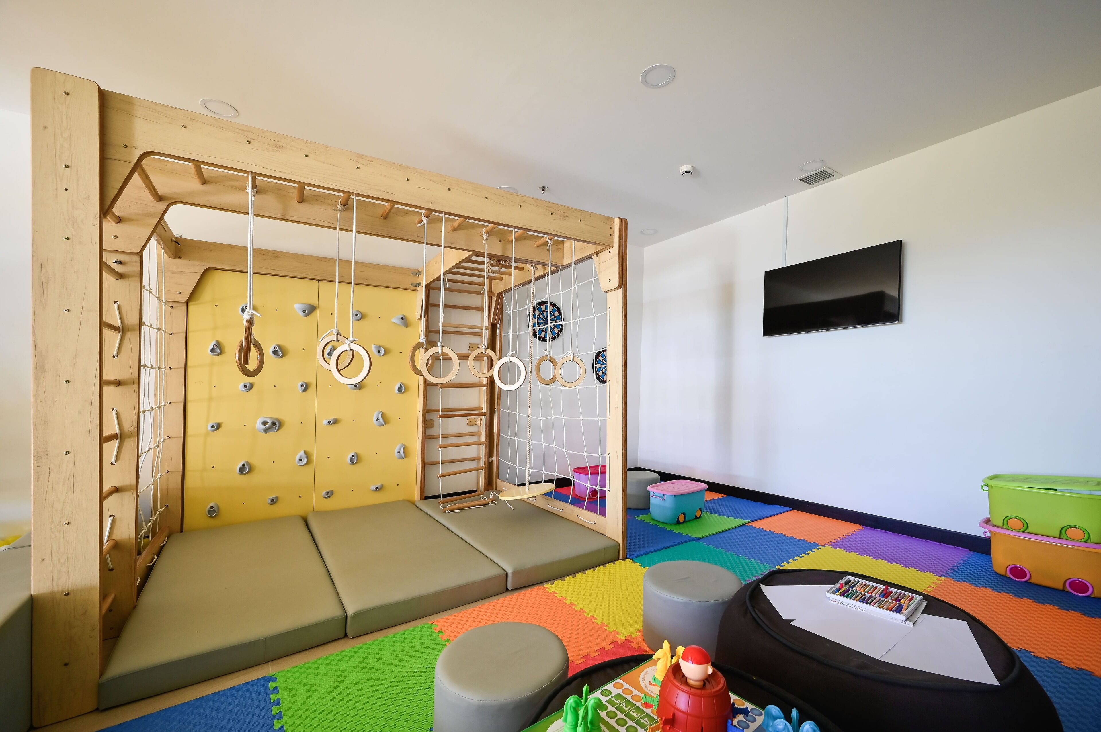 Una sala de juegos con una pared de escalada, suelo acolchado y un televisor en la pared.