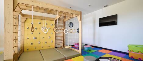 A playroom with a climbing wall, padded flooring, and a television on the wall.