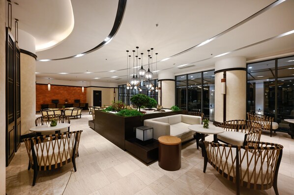 A modern lobby with round tables, wicker chairs, a central seating area, and a large window. - Emerald Ho Tram Resort (Ho Chi Minh City)