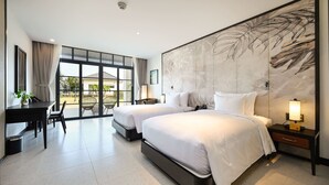 A modern hotel room with two beds, a desk, and a large window offering a view of the outdoors. - Emerald Ho Tram Resort (Ho Chi Minh City)