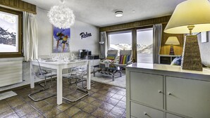 Een moderne kamer met een eettafel, stoelen, een groot raam met uitzicht op bergen, een kroonluchter en een kast.