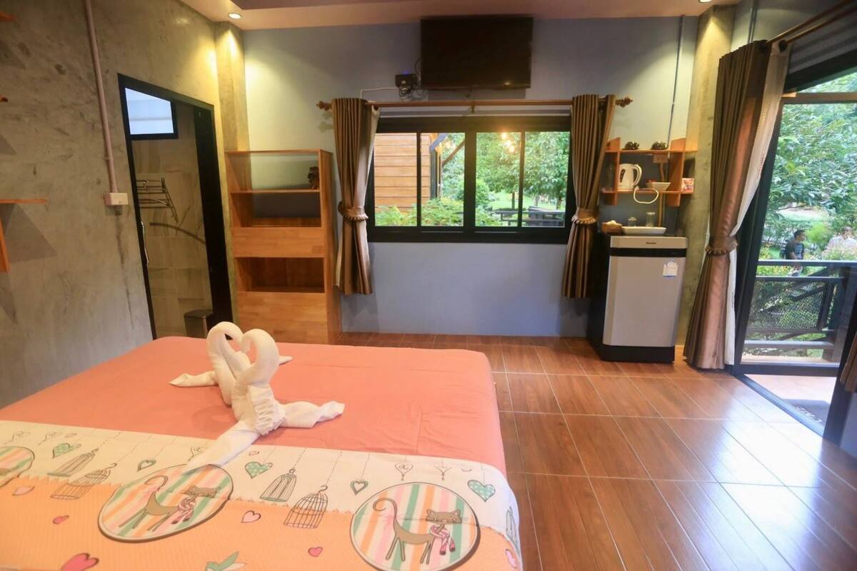 Hotelkamer met een bed, een kitchenette, een televisie en een balkon met uitzicht op groen.