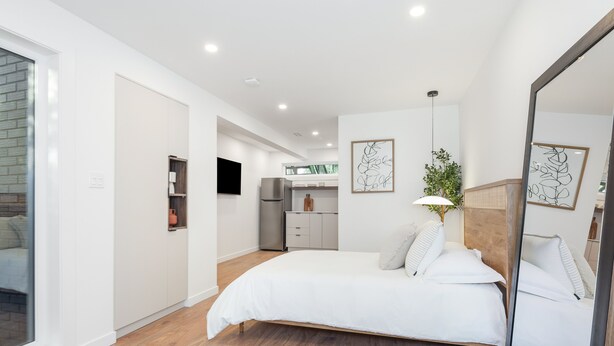 Een moderne slaapkamer met een groot bed, een spiegel en uitzicht op de keuken.