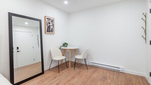 Een kamer met een houten vloer, een witte deur, een ronde tafel met twee stoelen en een klein plantje op de tafel.