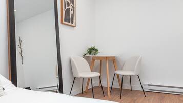 Ein modernes Zimmer mit einem Bett, einem spiegelnden Holzbettrahmen, einem kleinen Tisch mit zwei Stühlen und einem gerahmten Bild an der Wand.
