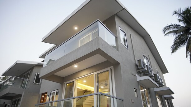 Un edificio moderno de varios pisos con un balcón destacado, amplios ventanales y una escalera visible que conduce al piso superior.