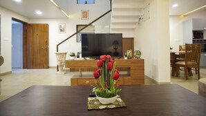 Una sala de estar moderna con un comedor de madera oscura, un jarrón blanco con flores rojas, un televisor de pantalla plana y una escalera que sube a un piso superior.