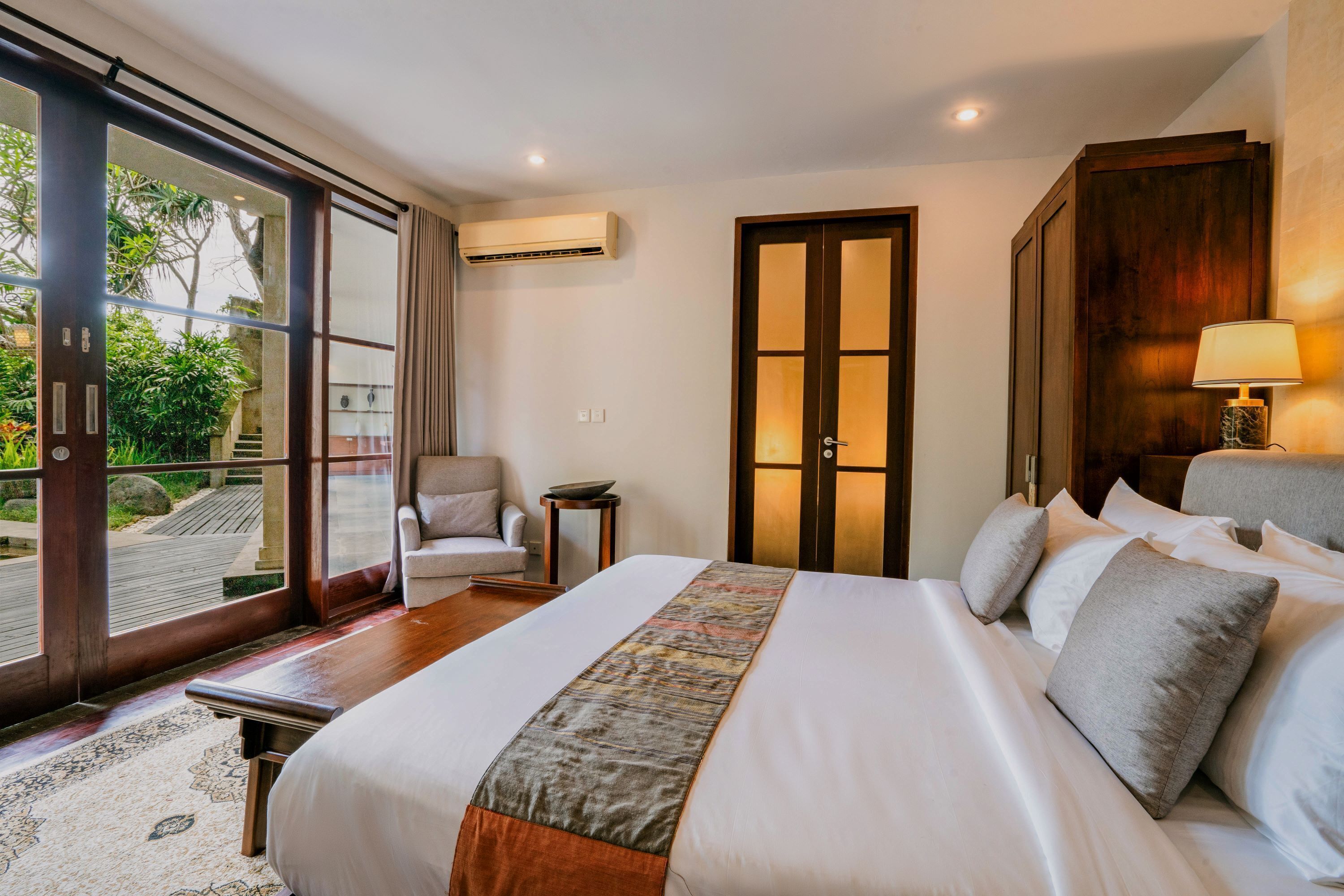 Ein Hotelzimmer mit einem großen Bett, einem Sessel, einem kleinen Tisch und Blick durch eine Glastür.