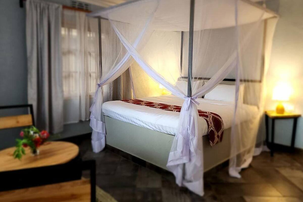 A single bed with a canopy, a bedside table with a vase of flowers, and a lamp on a nightstand.