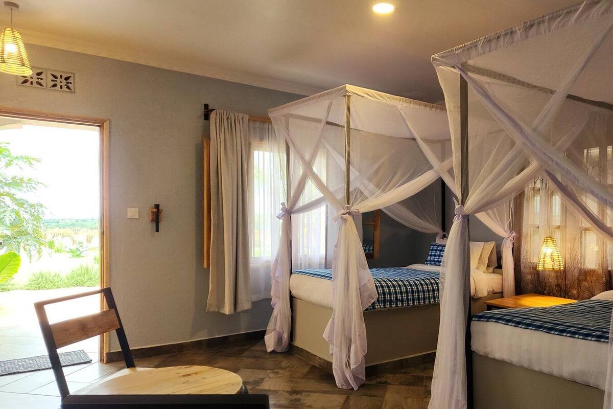 A room with two beds, each with a canopy. There is a chair and a table in the foreground.