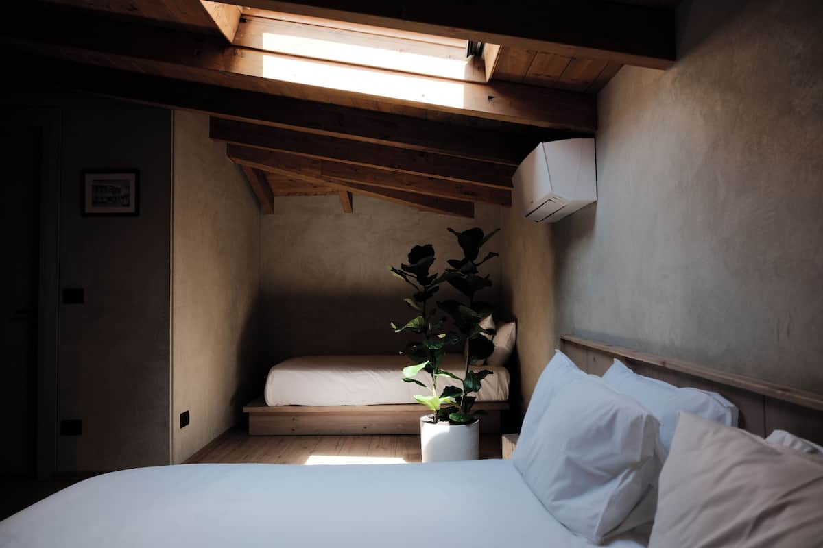Une chambre avec un plafond en bois, un lit avec une literie blanche, une plante en pot et un climatiseur fixé au mur.
