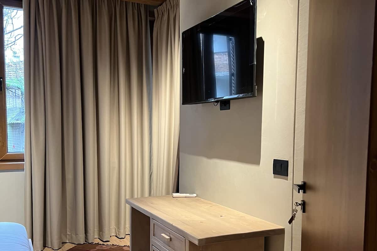 Une pièce comprenant un lit, un bureau en bois, un téléviseur fixé au mur et une porte.