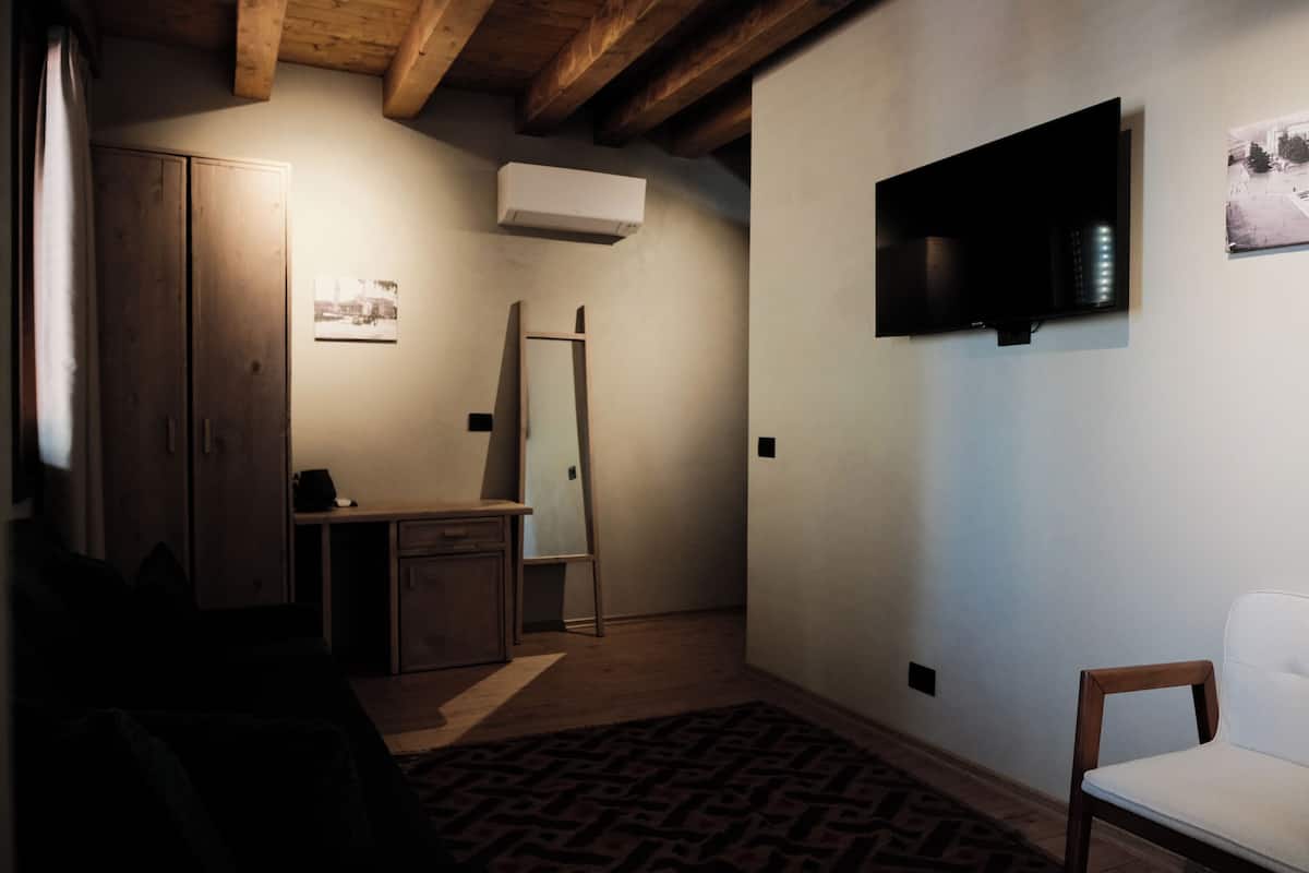 Une pièce avec un plafond en bois, un téléviseur à écran plat fixé au mur, un bureau avec une chaise, une armoire et un tapis à motifs.