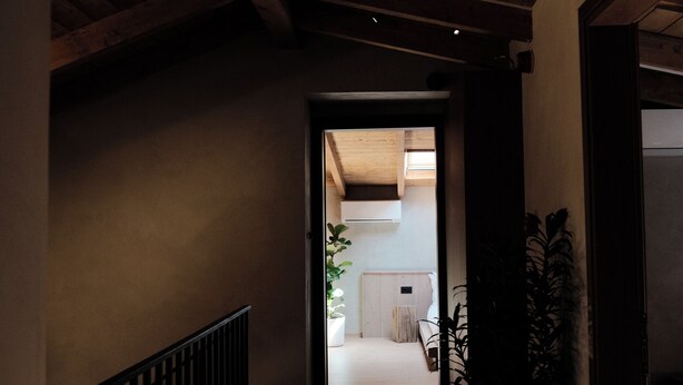 Un couloir doté d’un plancher en bois et d’une rambarde noire, qui mène à une pièce avec une porte et une plante.