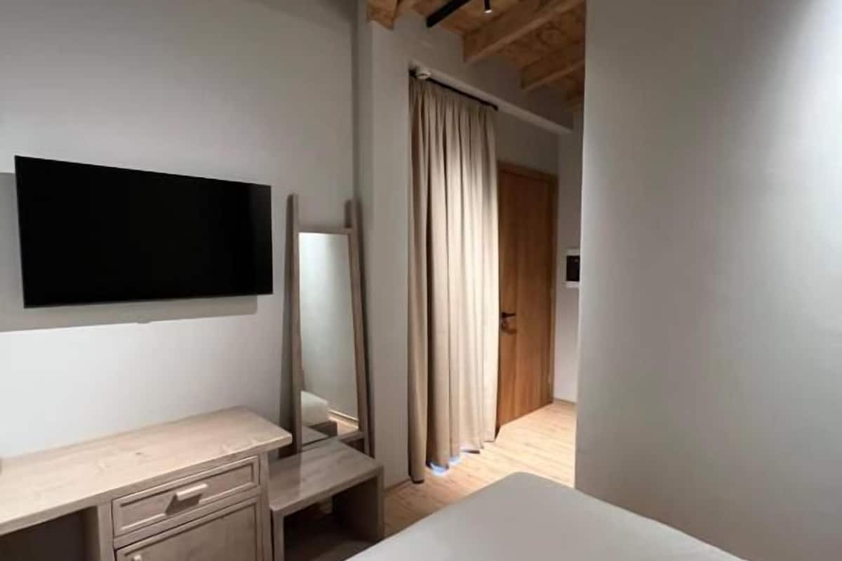 Une chambre avec un plafond en bois, un lit, une table de chevet, un miroir et un téléviseur fixé au mur.