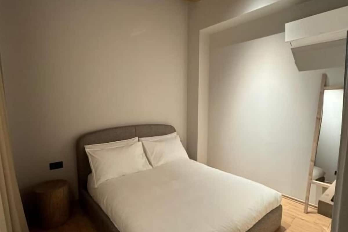 Une chambre avec un plafond en bois, un lit recouvert de linge de lit blanc et un petit tabouret rond.