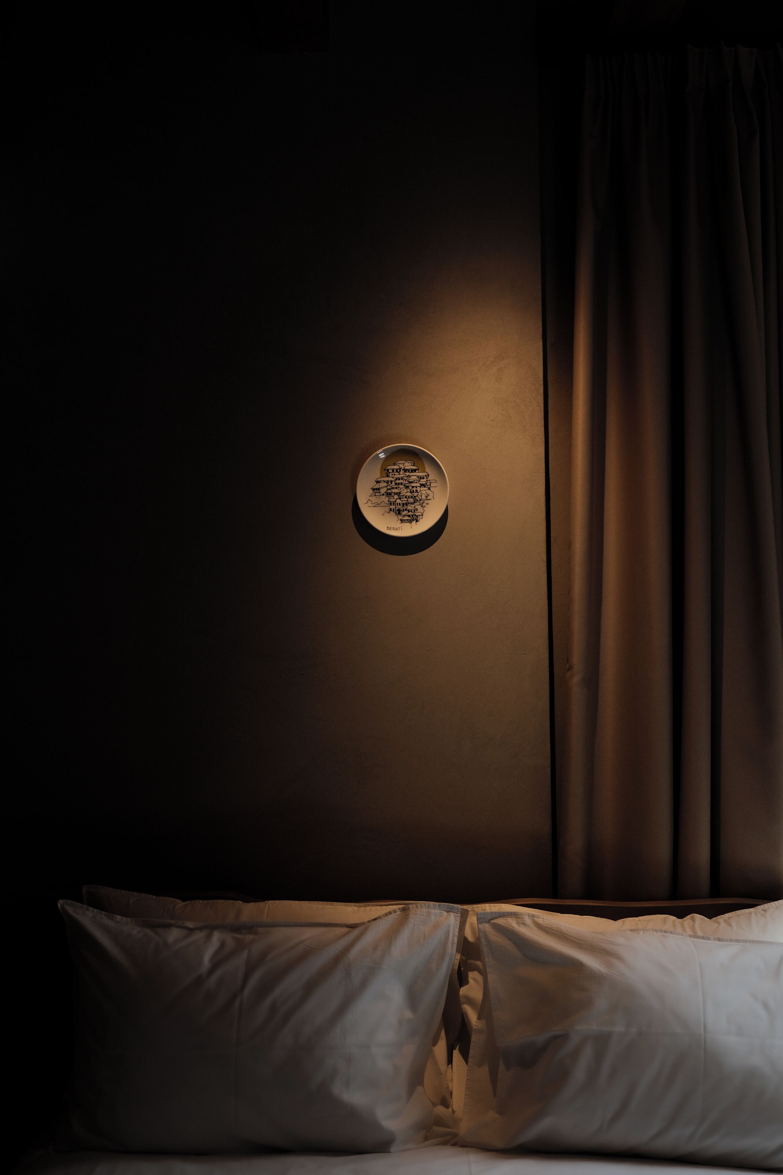 Een kamer met weinig licht, een bed, een wandplaat en een gordijn.