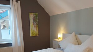 A bedroom with a bed, a nightstand, a lamp, and a window with curtains. - Ferienwohnung 2 für Max.4 Personen (Ruhpolding)