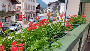 A balcony with potted geraniums, a street view with cars, and traditional buildings with balconies. - Ferienwohnung 2 für Max.4 Personen (Ruhpolding)