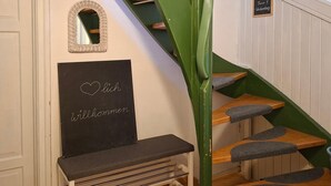 A staircase with green railings, a wooden bench, a mirror, and a sign reading 'Willkommen' in a room with wooden flooring and white walls. - Ferienwohnung 2 für Max.4 Personen (Ruhpolding)