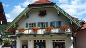 A traditional chalet with a balcony adorned with red flowers, a shop entrance, and a clear sky. - Ferienwohnung 1 für Max. 2 Personen (Ruhpolding)