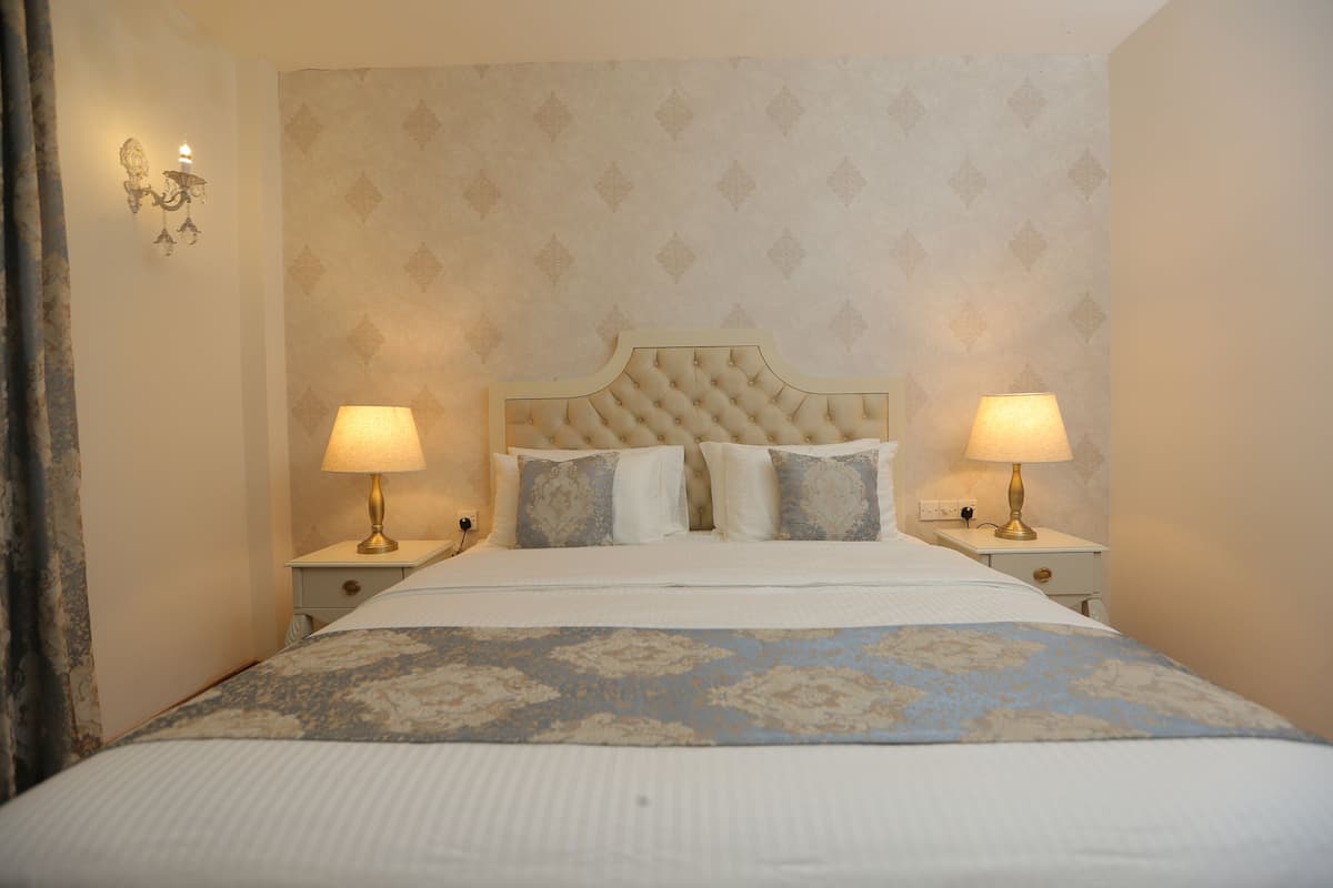 A neatly made bed with a floral bedspread, two bedside lamps, and a patterned wallpaper.