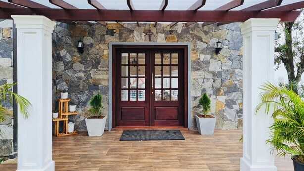 Una entrada revestida de piedra con una puerta de madera oscura, columnas blancas y plantas en macetas.