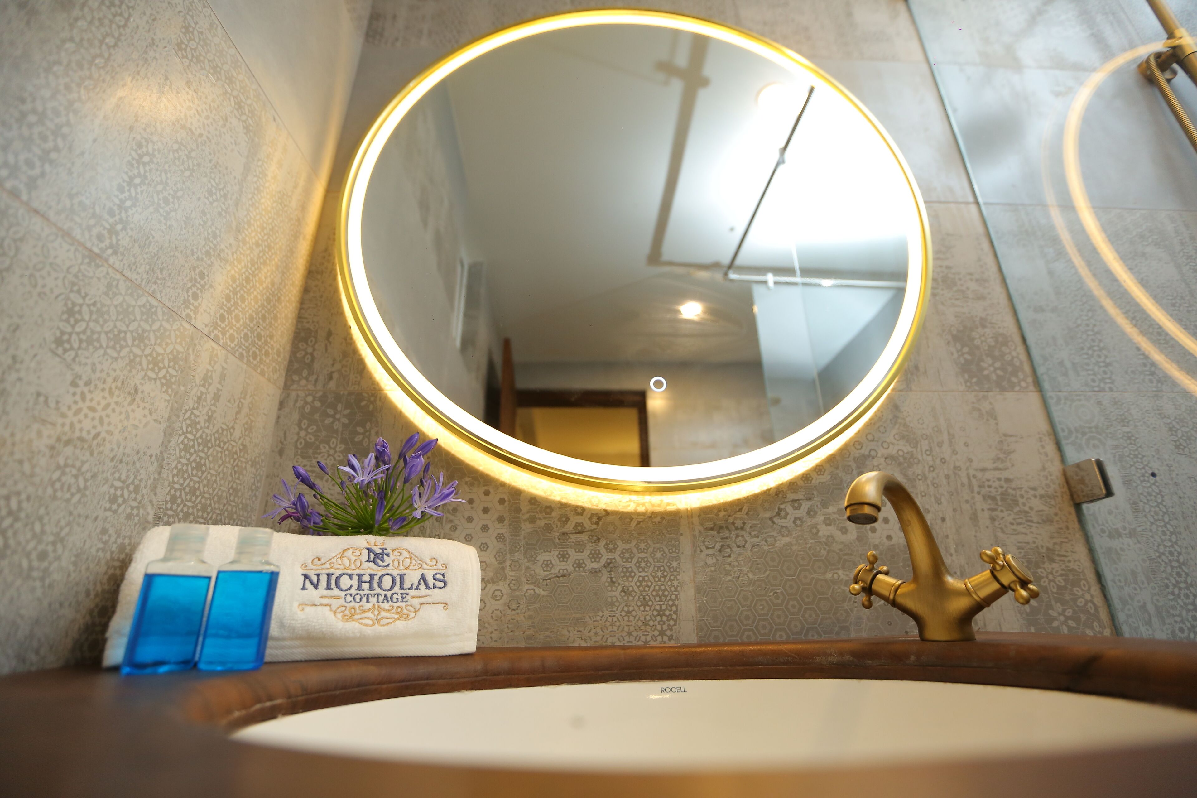 A bathroom with a round mirror, a sink, and a towel rack with a towel labeled "Nicholas Cottage".