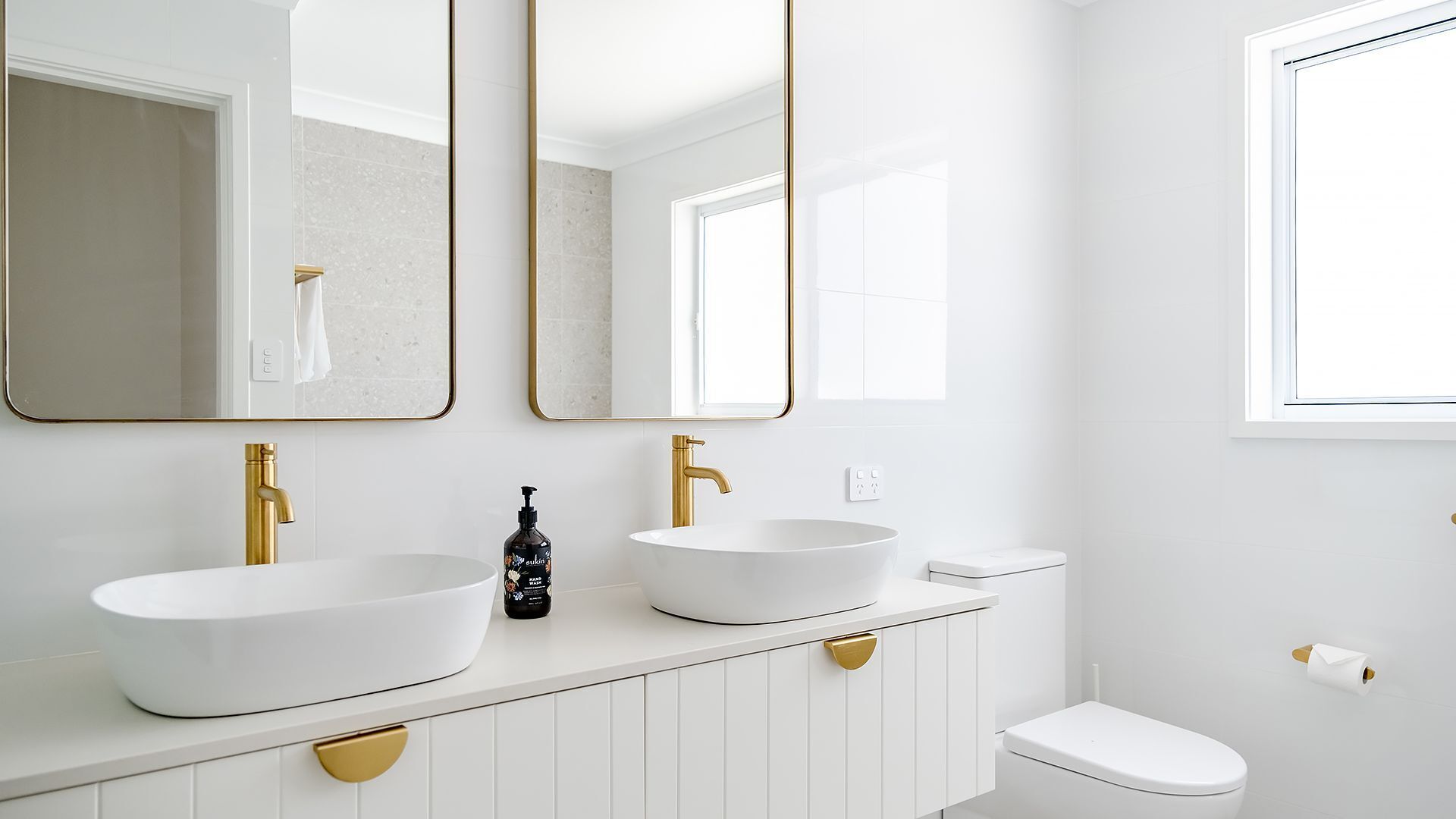 Une salle de bain moderne avec deux vasques, des robinets dorés et des toilettes blanches.