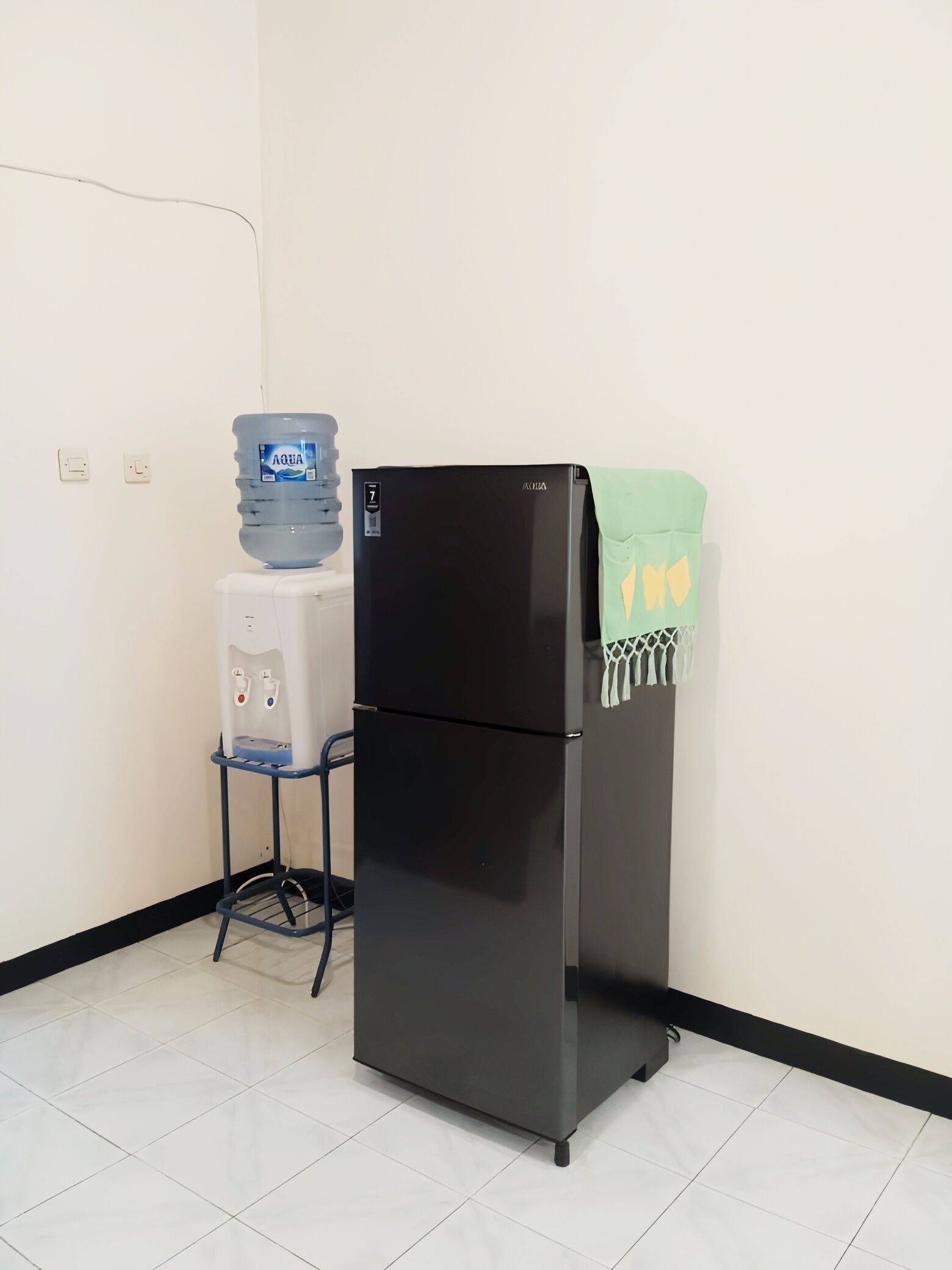 A black refrigerator with a green towel on top, a water dispenser, and a white water cooler.