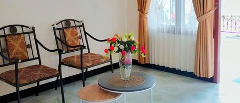 Una habitación con dos sillas, una mesita y un florero con flores.