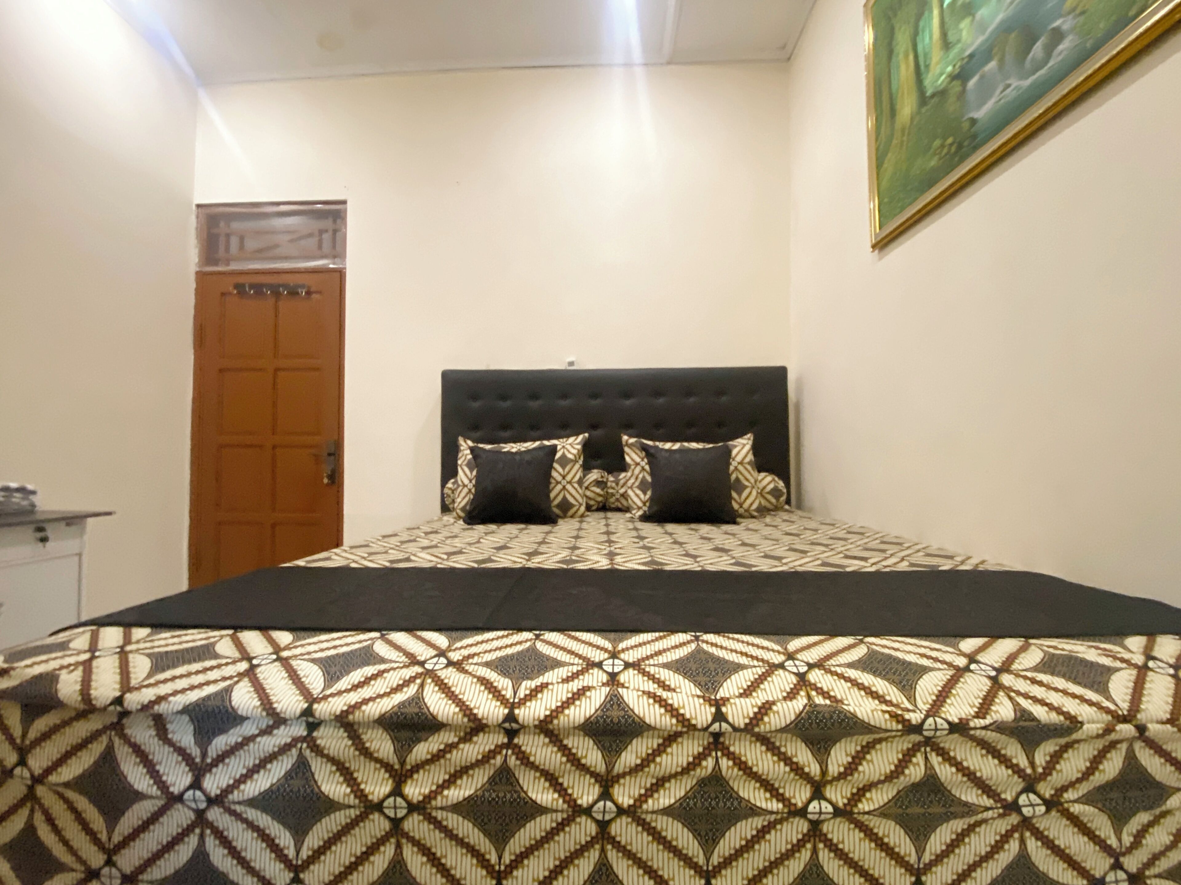 A bedroom with a patterned bedspread, a tufted headboard, and a door in the background.