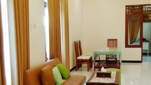 A spacious living room with a brown sofa, a coffee table, and a dining table with chairs. - Penginapan Prambanan TRISAN (Prambanan)