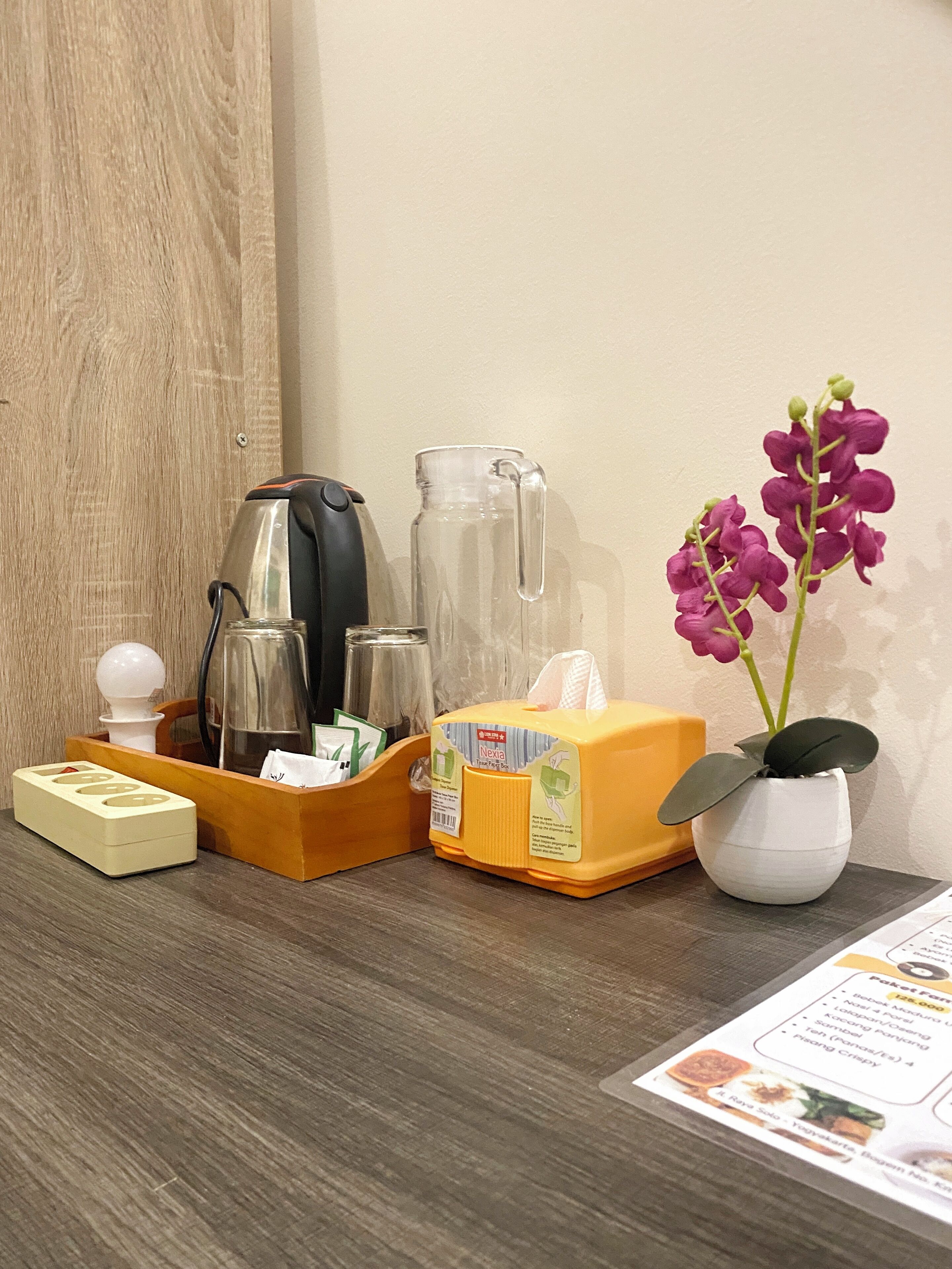 Ein Holztisch mit einer Kaffeemaschine, einem Glasbehälter, einer Taschentuchbox, einer kleinen Topforchidee und einer Speisekarte.