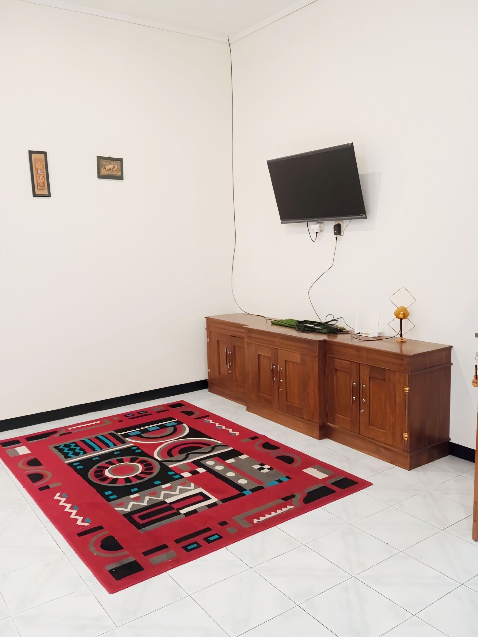 Een kamer met een wandgemonteerde flatscreen televisie, een houten kast en een kamerbreed tapijt met patroon.