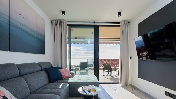 A modern living room with a grey sofa, a small round table with a glass top, and a flat-screen TV mounted on the wall. - Hedera Estate, Hedera A45 (Dubrovnik)