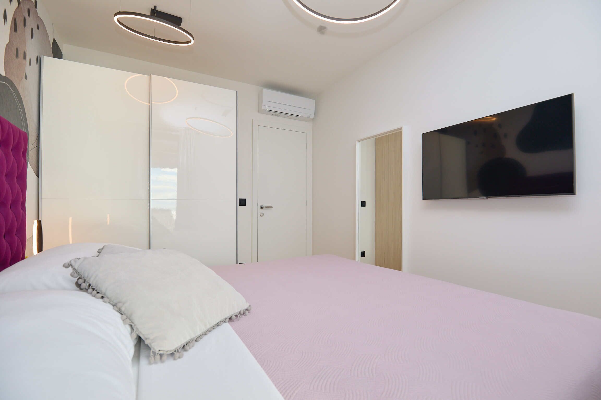 Een slaapkamer met een bed, een aan de muur bevestigde televisie en een airconditioning.