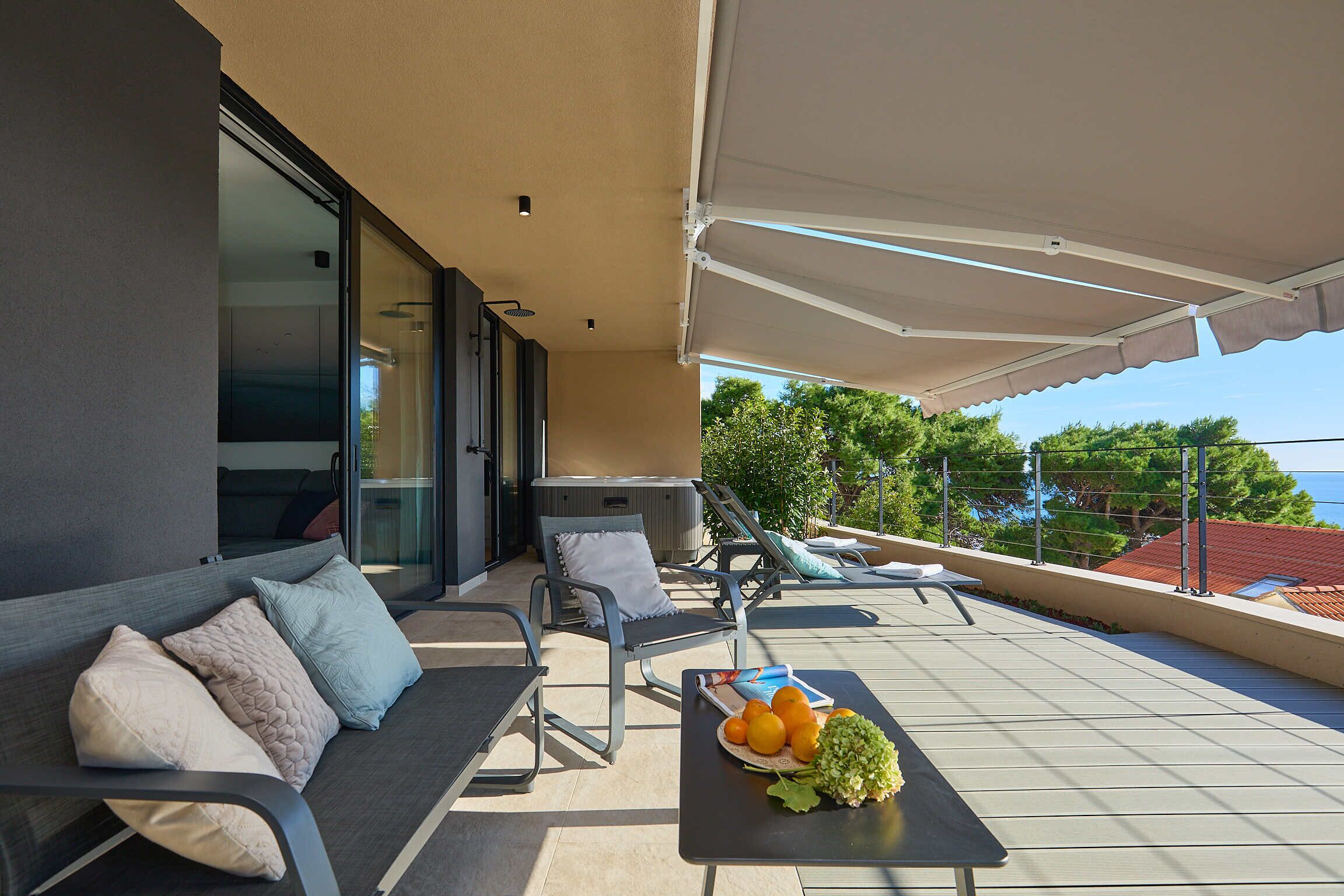 A balcony with a sofa, chairs, and a table with fruit.