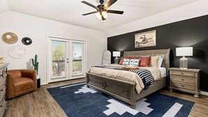 A bedroom with a bed, a ceiling fan, a nightstand, a lamp, a dresser, a chair, and a cactus.