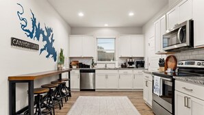 A modern kitchen with white cabinets, stainless steel appliances, and a bar area with stools.