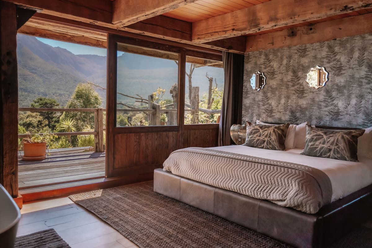 Ein Schlafzimmer mit einem großen Bett, Holzboden und Bergblick durch eine Schiebetür.