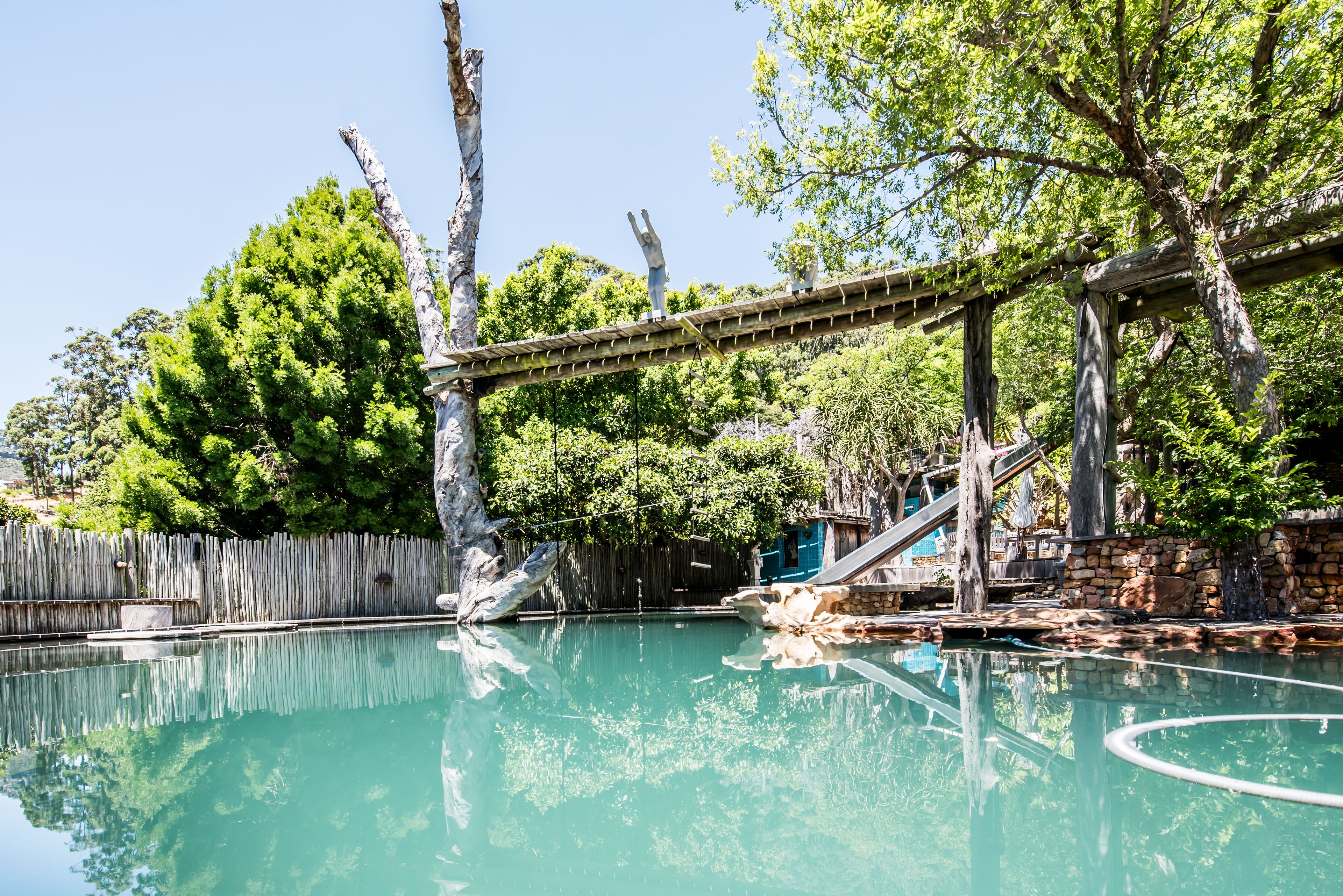 A pool area with a wooden bridge, stone structures, and lush greenery.