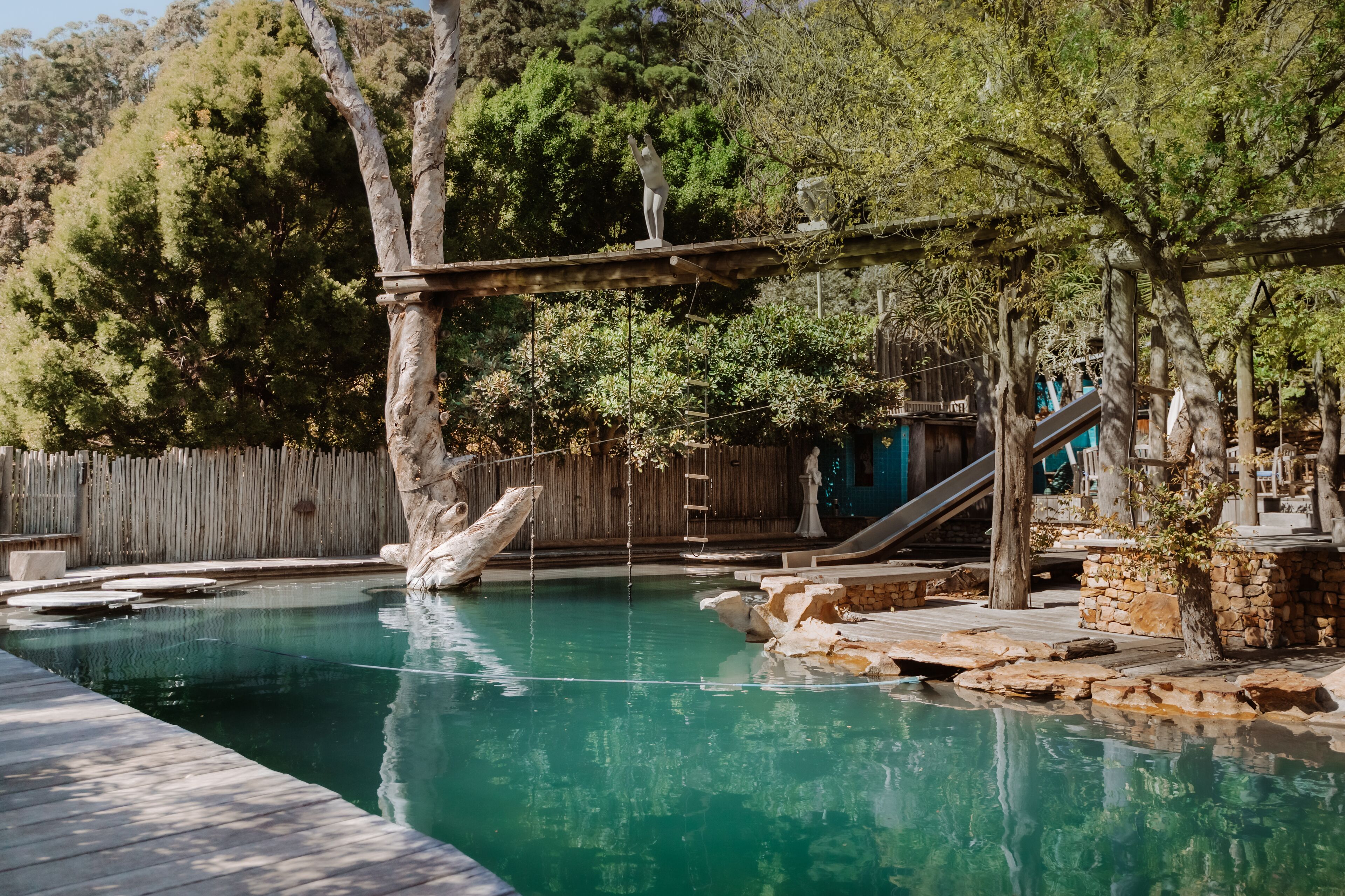 A swimming pool with a wooden deck, stone structures, and a wooden fence.
