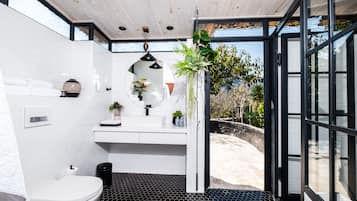 Un baño moderno con inodoro blanco, baldosas hexagonales negras en el suelo, un lavabo blanco con espejo y un cubo de basura negro.