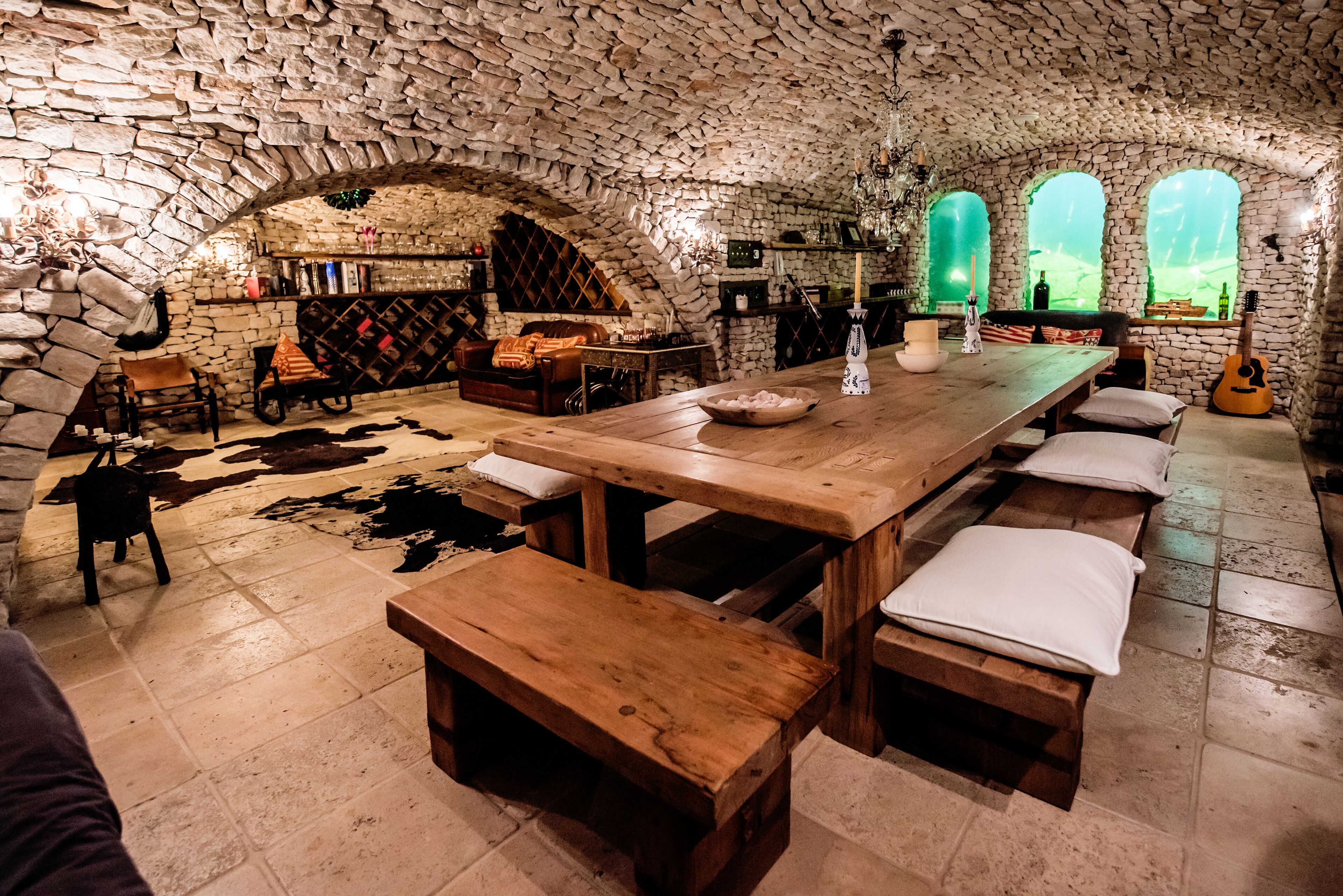 Une pièce rustique aux murs de pierre, avec une longue table en bois, des bancs et un tapis en peau de vache.