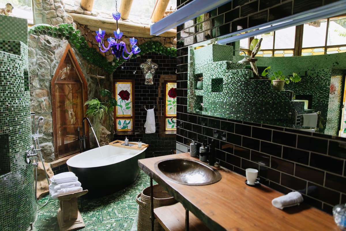 Ein Badezimmer mit freistehender Badewanne, einem hölzernen Waschtisch und einer grünen Mosaikwand.