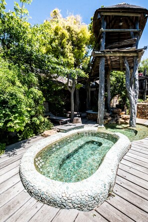 A wooden deck with a stone-lined hot tub surrounded by lush greenery and a wooden structure. - Wonderland Cape Town (Cape Town)
