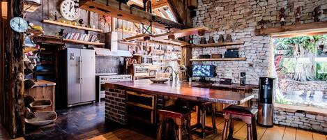 A rustic kitchen with wooden beams, stone walls, and a large island with stools.