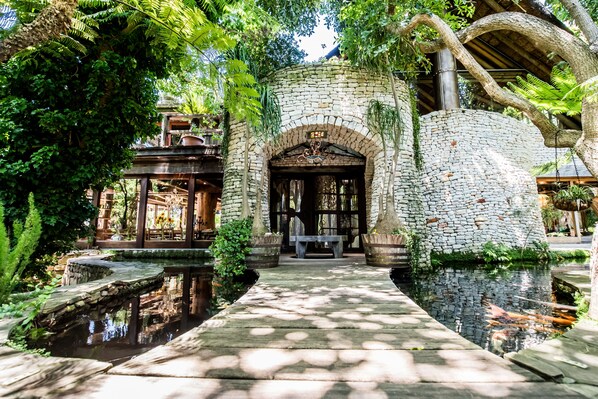 A stone archway leading to a wooden bench and a small pond, surrounded by lush greenery. - Wonderland Cape Town (Cape Town)