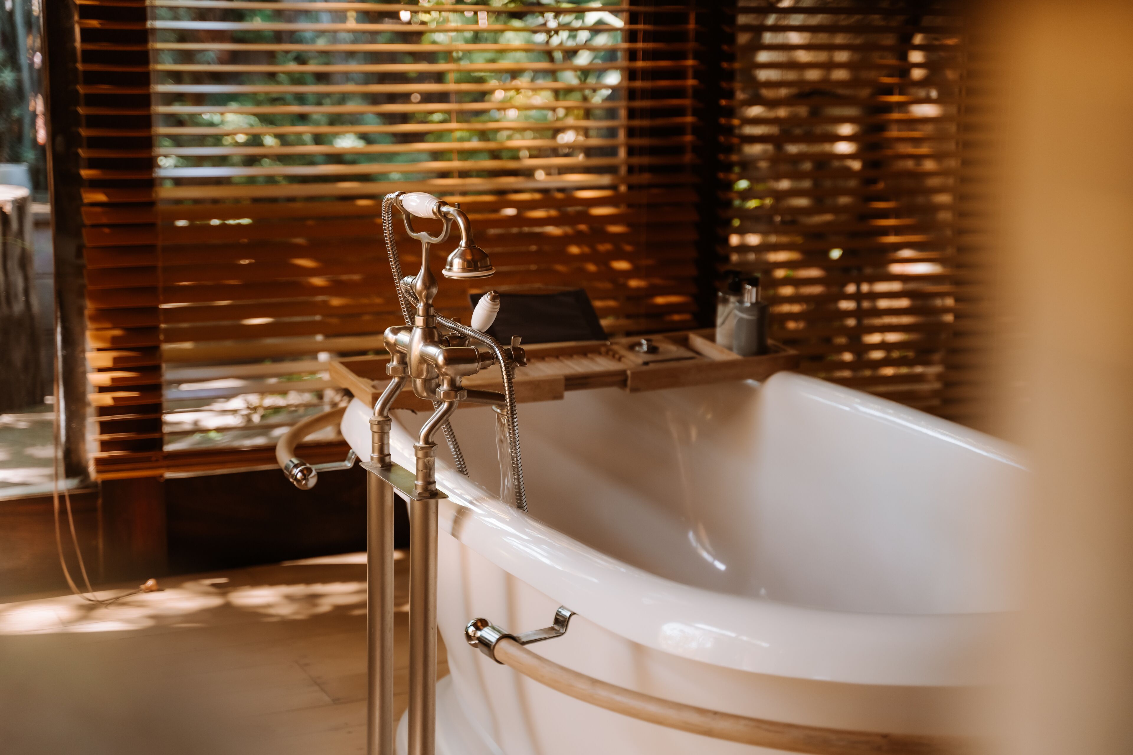 Un baño moderno con una bañera independiente, persianas de madera y un toallero a la vista.